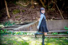 a woman in black dress and knee high boots standing on grass with trees behind her