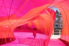 a woman standing in front of an orange structure with pink fabric covering it's walls