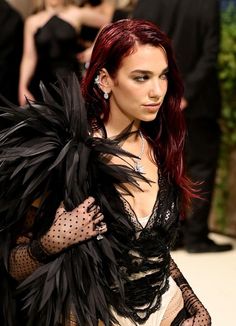 a woman with red hair and black feathers on her arm, wearing a sheer dress