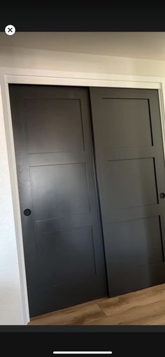 an empty room with two black doors and wood flooring on the side of it