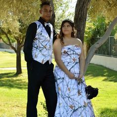 a young man and woman dressed in formal wear standing next to each other under a tree