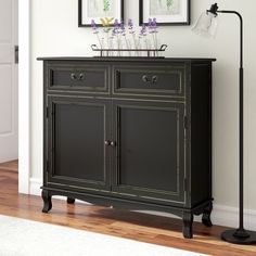 a black sideboard with flowers on top and two framed pictures above it