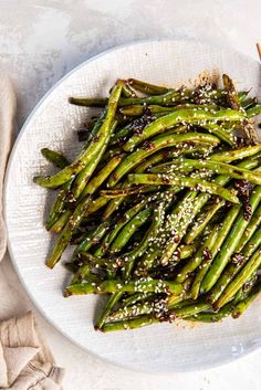 asparagus with sesame seeds on a white plate next to chopsticks and napkin