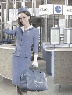 a woman in an airplane attendant's uniform is holding a handbag and posing for the camera