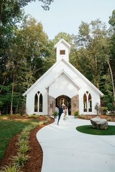 a bride and groom are standing in front of a white church with trees around them