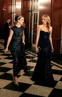 two women dressed in evening gowns walking down a hall together, one wearing a black dress