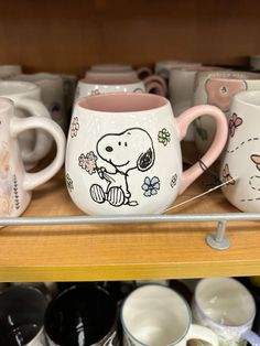 many coffee mugs are sitting on the shelf in front of each other, one has a cartoon character painted on it