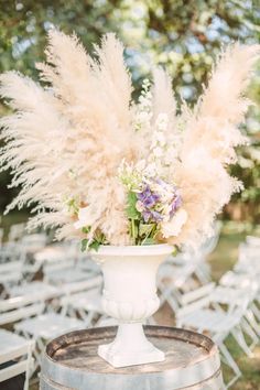 a vase filled with lots of flowers sitting on top of a wooden barrel next to chairs