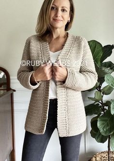 a woman standing in front of a potted plant wearing a cardigan sweater and jeans