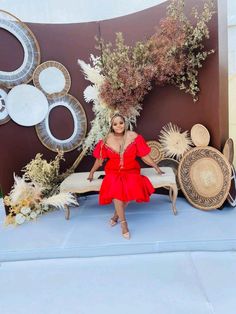 a woman in a red dress sitting on a bench surrounded by decorative objects and flowers