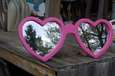 a pair of pink heart shaped sunglasses sitting on top of a wooden table next to a mirror