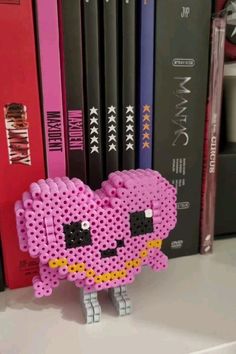 a pink beaded heart sitting on top of a book shelf next to some books