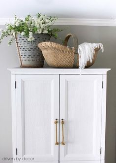 a white cabinet with baskets and flowers on top