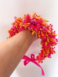 a hand holding a pink and orange wreath