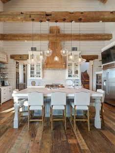 a large kitchen with wooden floors and white chairs around a dining table that is surrounded by hanging lights