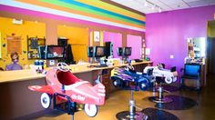 the interior of a children's hair salon with toys on tables and colorful walls