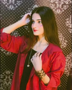 a woman with long hair wearing a red shirt and bracelets standing in front of a wall