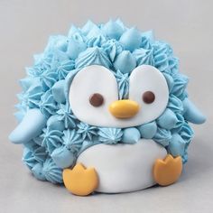 a blue and white cake with a little penguin on it's face, sitting in front of a gray background