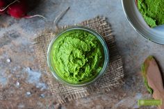 a glass jar filled with green food next to radishes and a wooden spoon