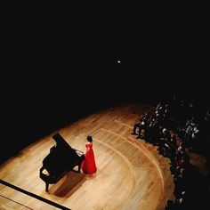 a woman in a red dress standing next to a black piano on top of a stage