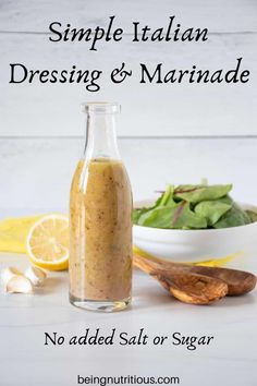 a bottle filled with dressing next to a bowl of salad and wooden spoon on a white table