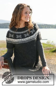 a woman sitting on top of a wooden bench next to the ocean wearing a black and white sweater