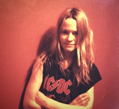 a man with long hair standing in front of a red wall wearing a black shirt