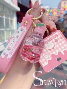 a hand holding a pink keychain with hello kitty on it and an empty bottle in the middle