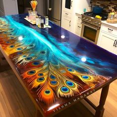 a kitchen island with a painted peacock feather design on the top and bottom, in front of an oven