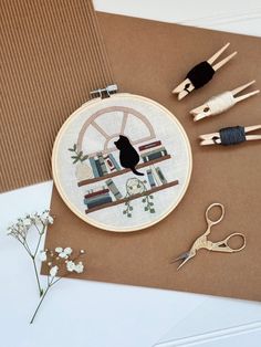 a cat sitting on top of a book shelf next to some scissors and thread spools