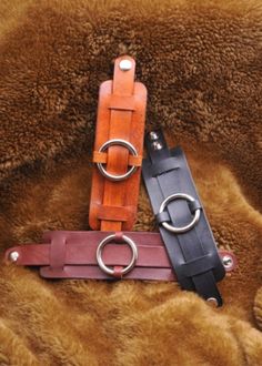 two leather belts with rings on them sitting on a fur covered surface in the sun