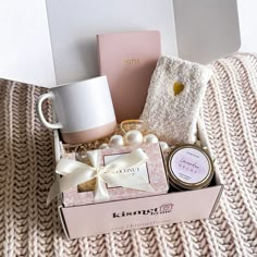 a pink box with some items in it sitting on a blanket next to a mug