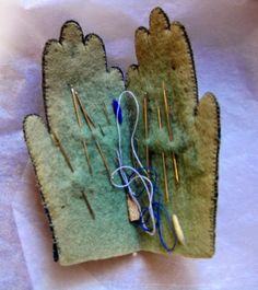 a pair of gloves sitting on top of a piece of cloth with needles sticking out of it