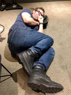 a man is sitting on the floor with his hands in his mouth and wearing glasses