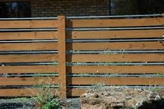 a wooden fence is shown in front of a brick building with grass growing on the ground