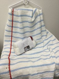 a white and blue blanket with a red string hanging from it's end on a hanger