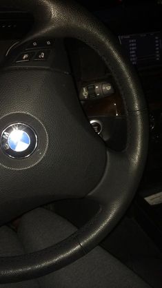 the steering wheel and dashboard of a car with black leather trims, including an emblem on the center console