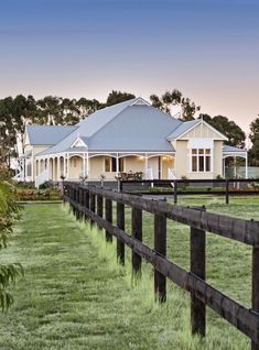 a large white house sitting in the middle of a lush green field next to a wooden fence