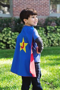 a young boy dressed up as a super hero standing in the grass wearing a cape