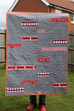 a person holding up a quilt in front of a house with red shoes on the grass