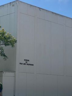 two people are standing in front of a large white building with writing on the side