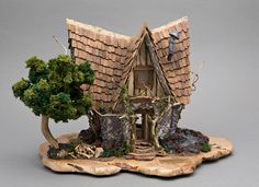 a miniature house made out of tree stumps and rocks with a man on the roof