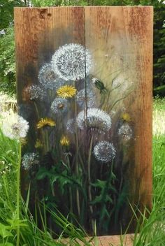 a painting of dandelions on a wooden block in the grass with trees in the background