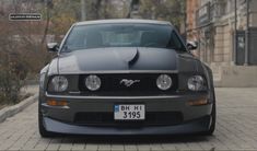 the front end of a grey mustang parked on a brick sidewalk in an urban area