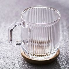 a clear glass coffee mug sitting on top of a wooden coaster with a handle and ring