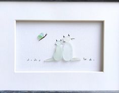 two white birds sitting next to each other in a shadow box with a green butterfly on it