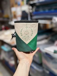 a hand holding up a cup with a green and white design on the side, in front of other items