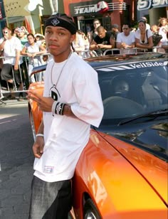 a young man standing next to a car in front of a large group of people