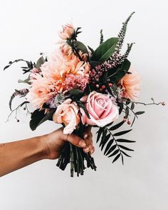 a person holding a bouquet of flowers in their left hand, against a white background