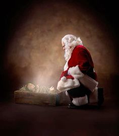 a man dressed as santa claus kneeling next to a box with a baby in it